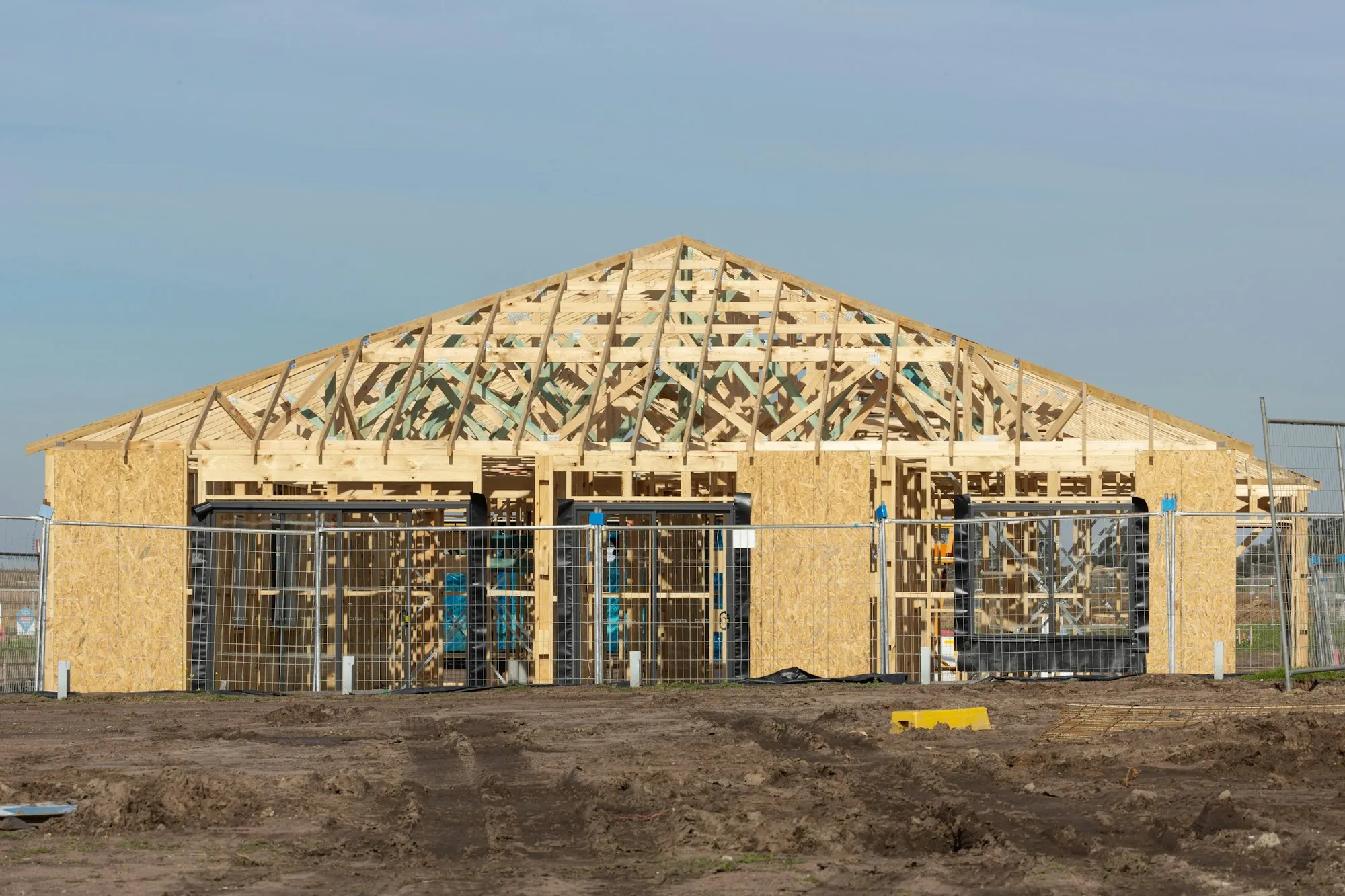 Wood-framed house on a dirt lot with roof trusses in place